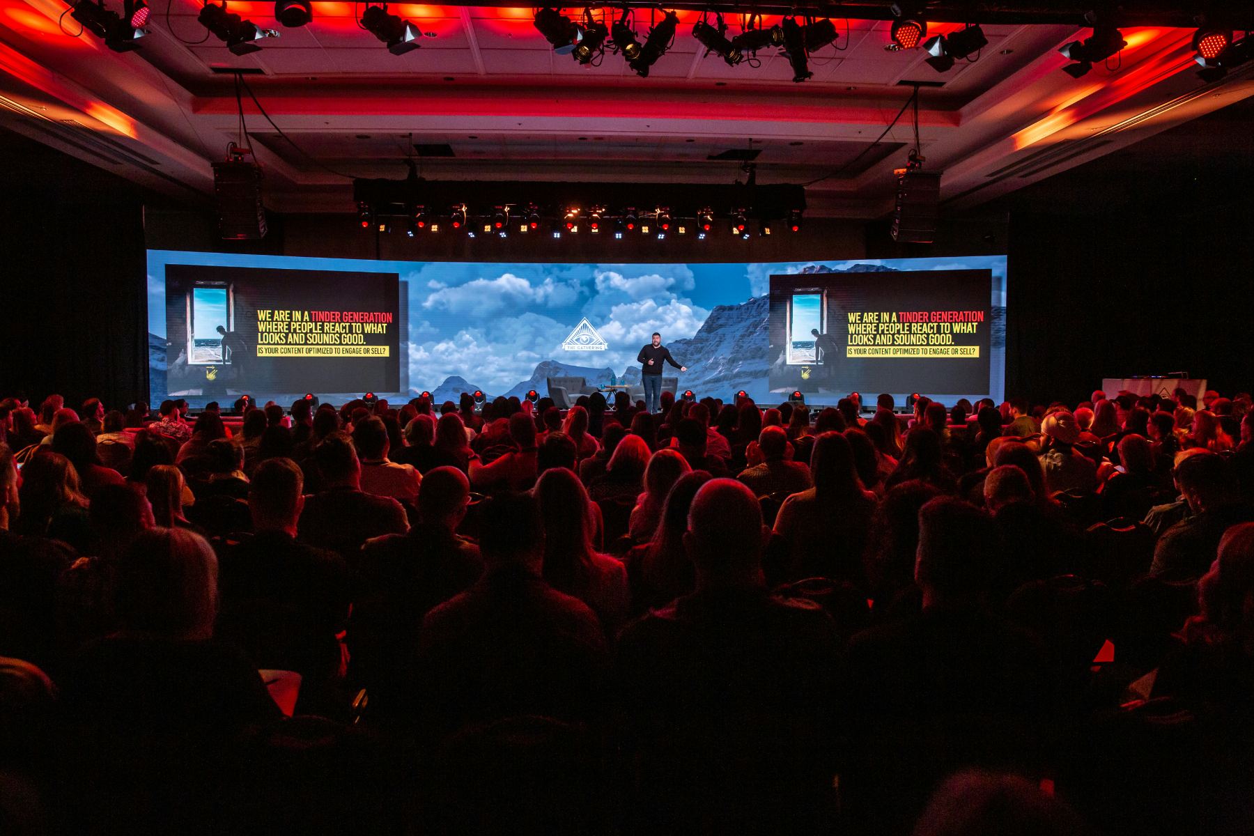A darkened auditorium of attendees facing a wide presentation screen.