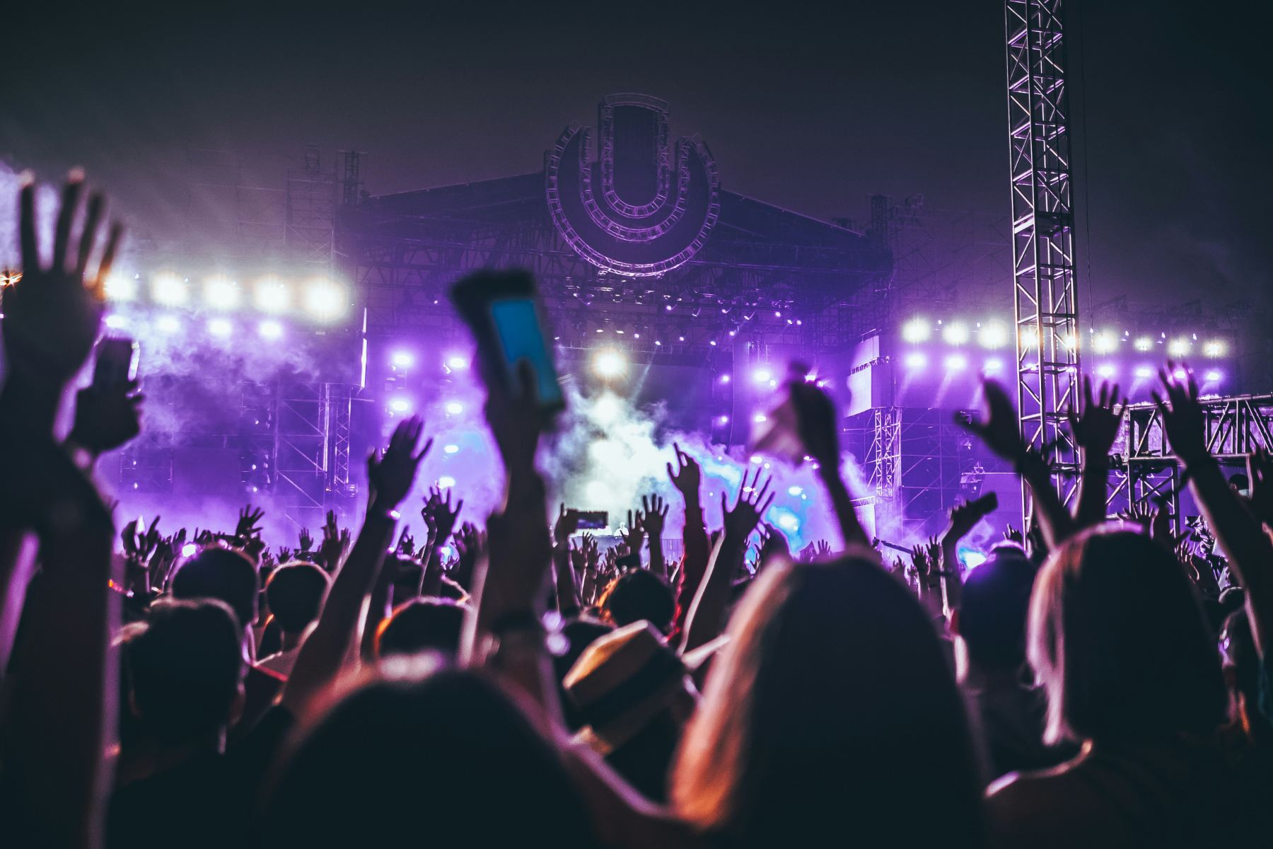 A festival crowd with raised hands in front of a lit main stage.