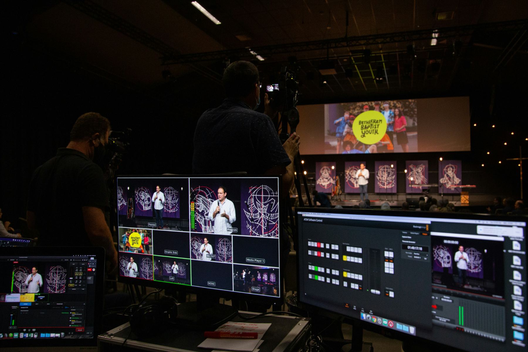 A sound engineer in headphones at a lit mixing desk, facing a stage rig from front of house.