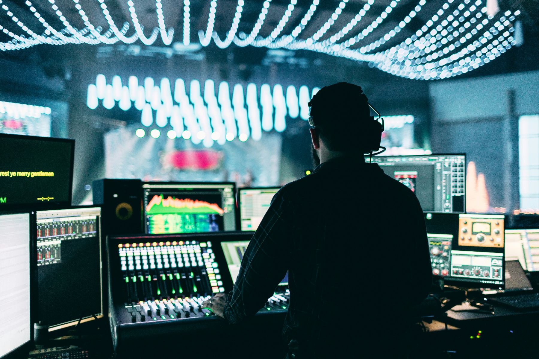 Two crew at a multi-camera position, a multiview of preview and programme feeds beside a vision-mixing panel.