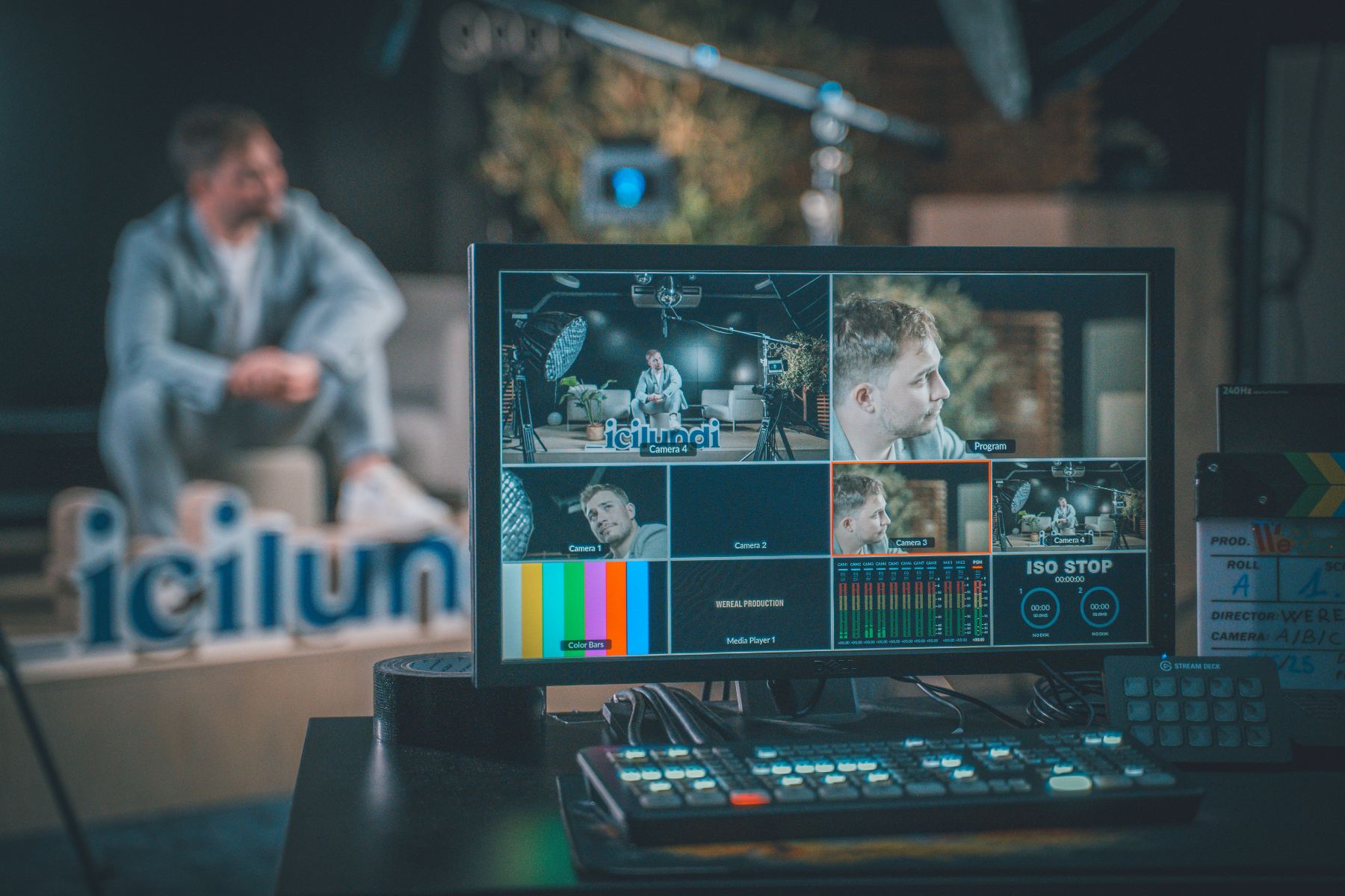 An operator at a desk watching a multiview of camera feeds and lyric graphics while a band plays on the stage beyond.